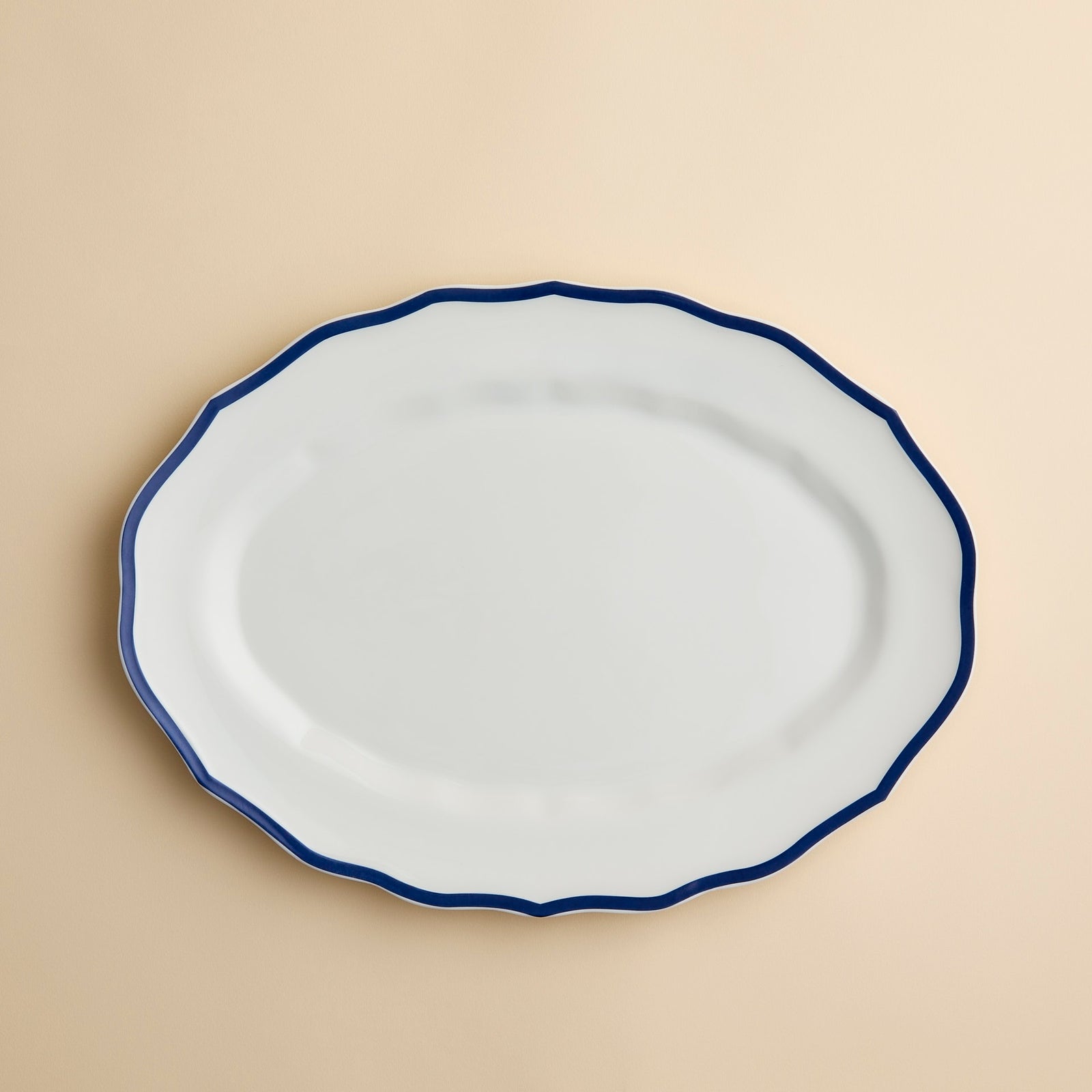 Stella Blue Scalloped Platter, an oval high-fired porcelain platter with a scalloped edge and a dark blue rim.