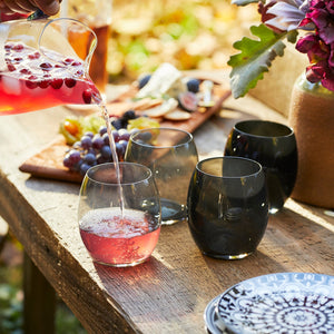 A person pouring red liquid into Les Nuages Gray Ombré Glasses Set of 4 tumblers by Caskata.