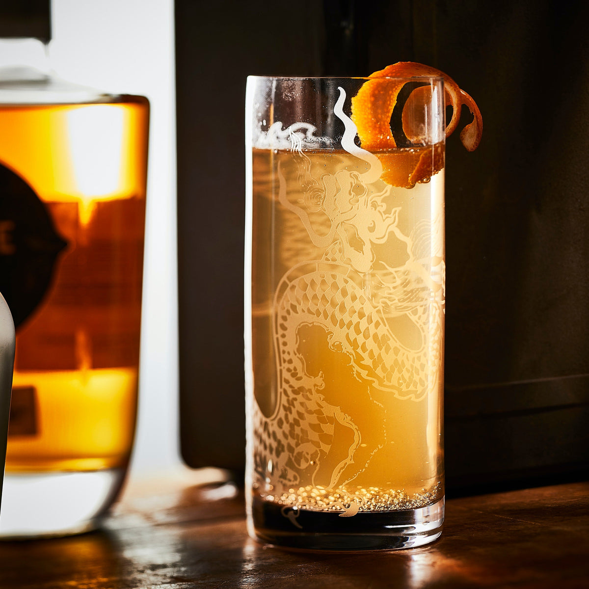 A thirst quenching cocktail topped with orange peel is featured in a sand etched highball glass by dragon design by Caskata.
