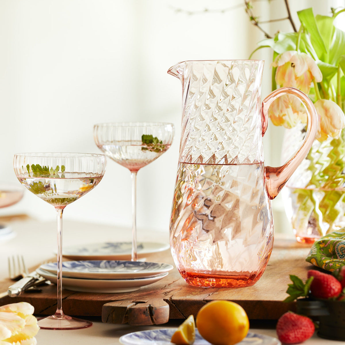 The mouth-blown crystal Quinn Rose Pitcher by Caskata is shown here with a pair of Quinn Rose Coupe Glasses as part of a sunny spring brunch scene.