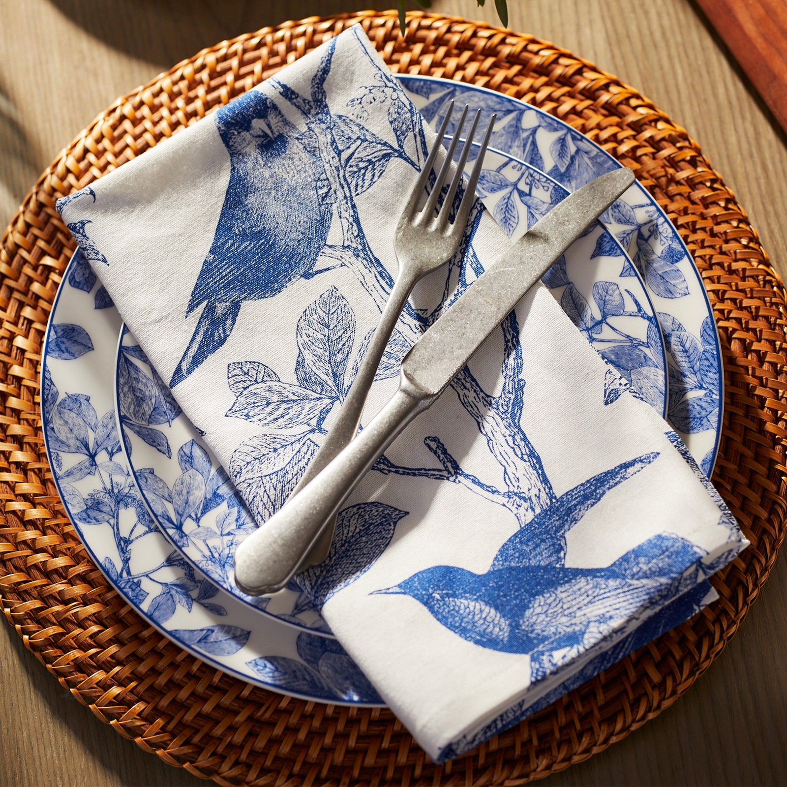 The Arbor Birds Blue Dinner Napkins by Caskata are a set of five white, 100% cotton napkins adorned with a blue Arbor pattern of perched birds and branches. Machine washable, they add elegance to any setting.