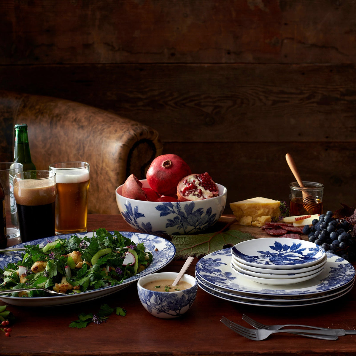 A vintage table filled with a combination of Caskata Artisanal Home&#39;s Blue Arbor Vegetable Serving Bowls, porcelain plates, bowls, glasses, and utensils.