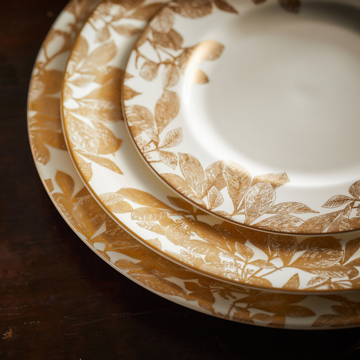 A stack of Arbor Rimmed Salad Plates Gold adorned with exquisite gold leaves, dishwasher safe. The brand name for these plates is Caskata Artisanal Home.