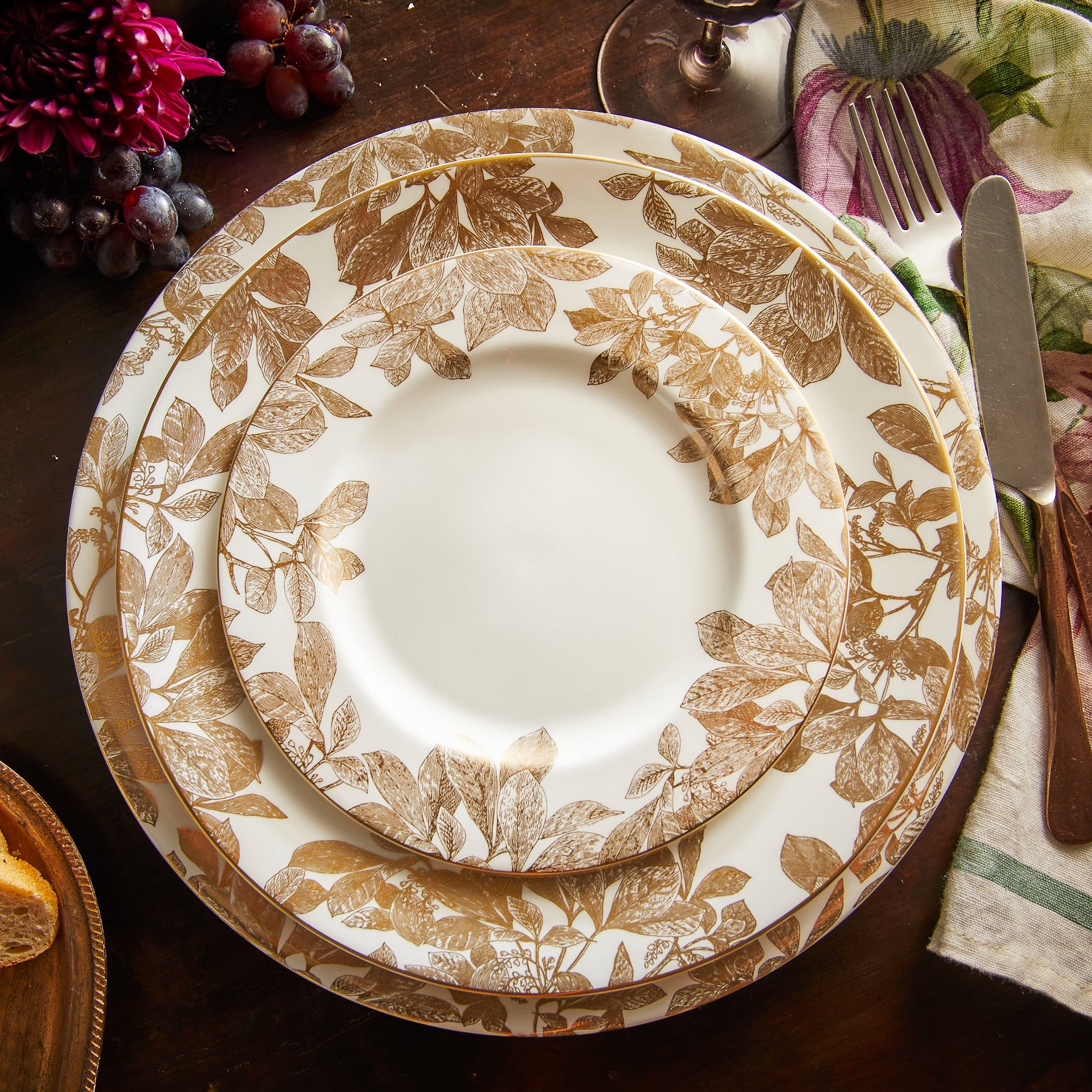A Caskata Artisanal Home Arbor Gold Rimmed Charger with gold leaf pattern botanical details around the edge.