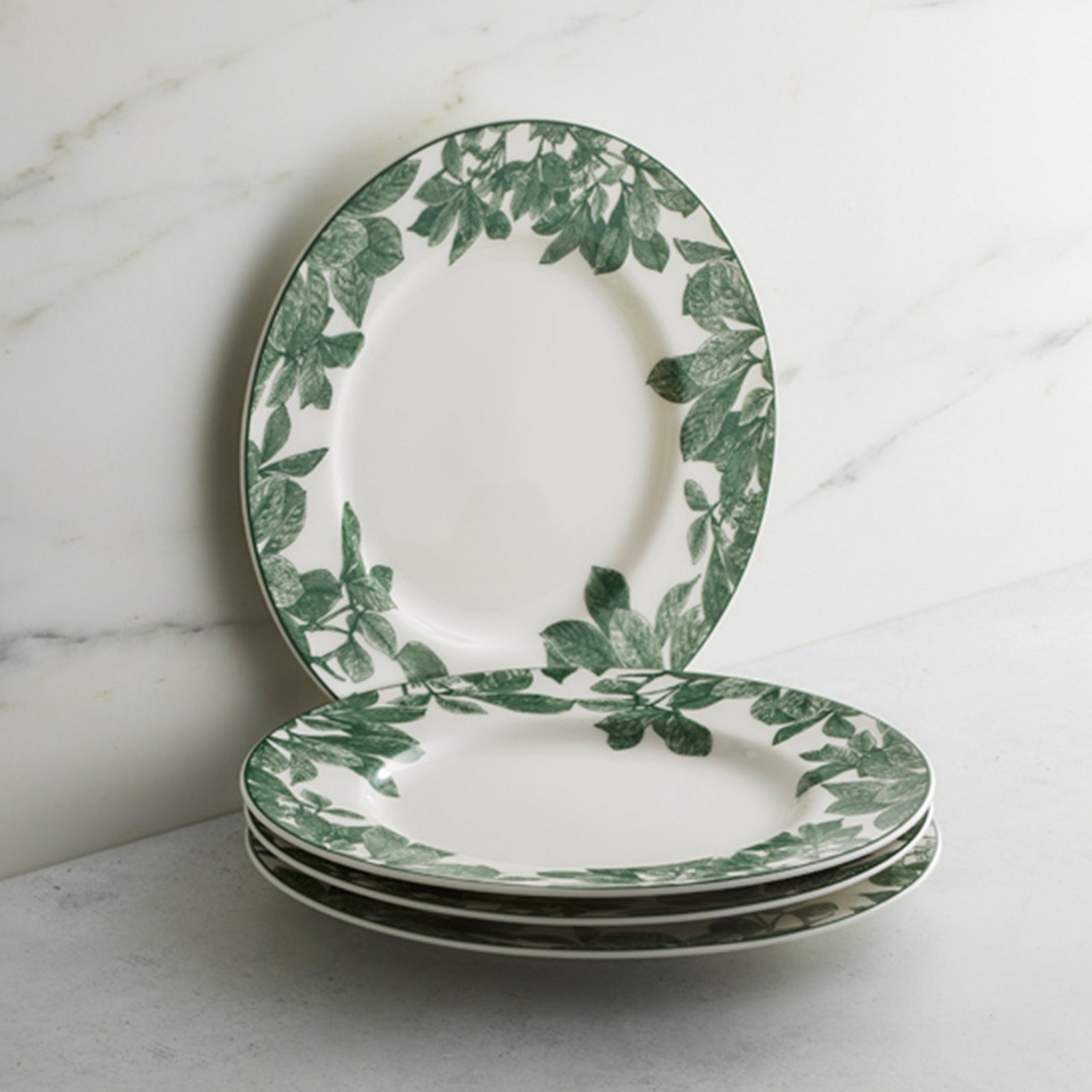 The Arbor Green Rimmed Salad Plate by Caskata, crafted from high-fired porcelain and featuring a green leafy pattern around the rim, is shown placed on a beige background.