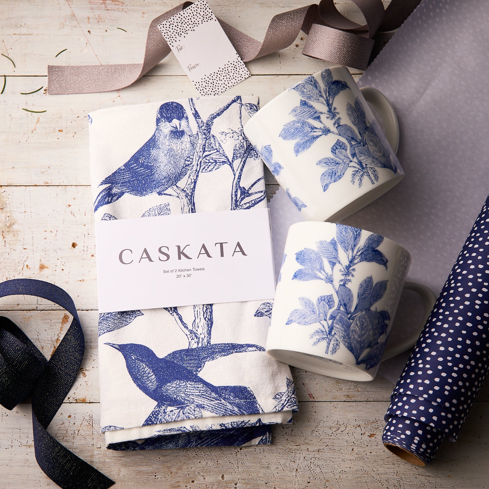 The "Arbor In the Kitchen" Bundle by Caskata features two blue botanical porcelain mugs and themed kitchen towels, beautifully arranged with ribbon and wrapping paper for a charming gift set.
