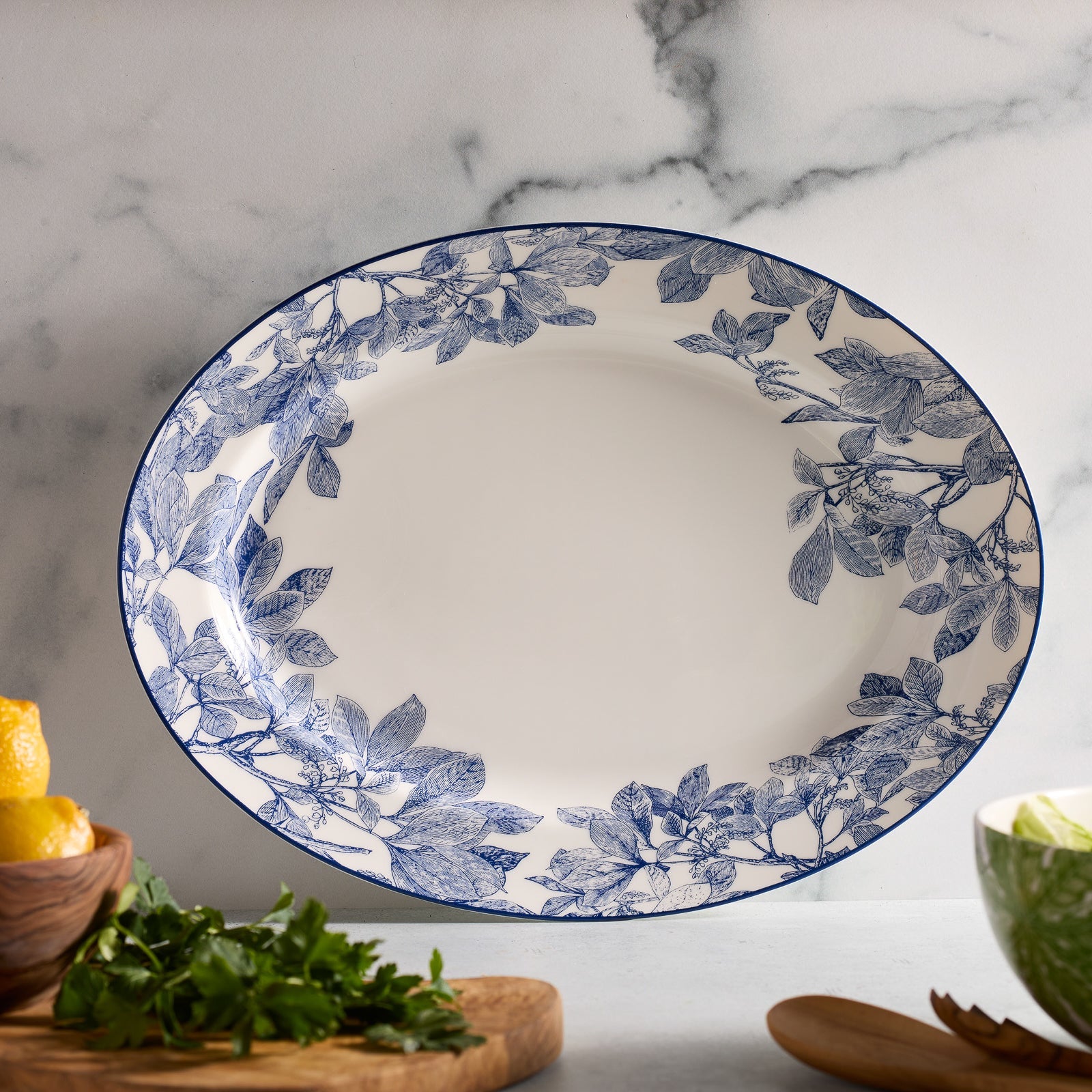 The Caskata Arbor Serving Set includes a white porcelain vegetable bowl and large oval platter, both featuring elegant blue leaf patterns along the edges.
