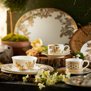 An arrangement featuring the elegant Hawthorne Gilt Cup & Saucer Set of 4 by Caskata Artisanal Home, surrounded by moss, flowers, and wooden decorations, evokes the intricate charm of delicate filigree jewelry.