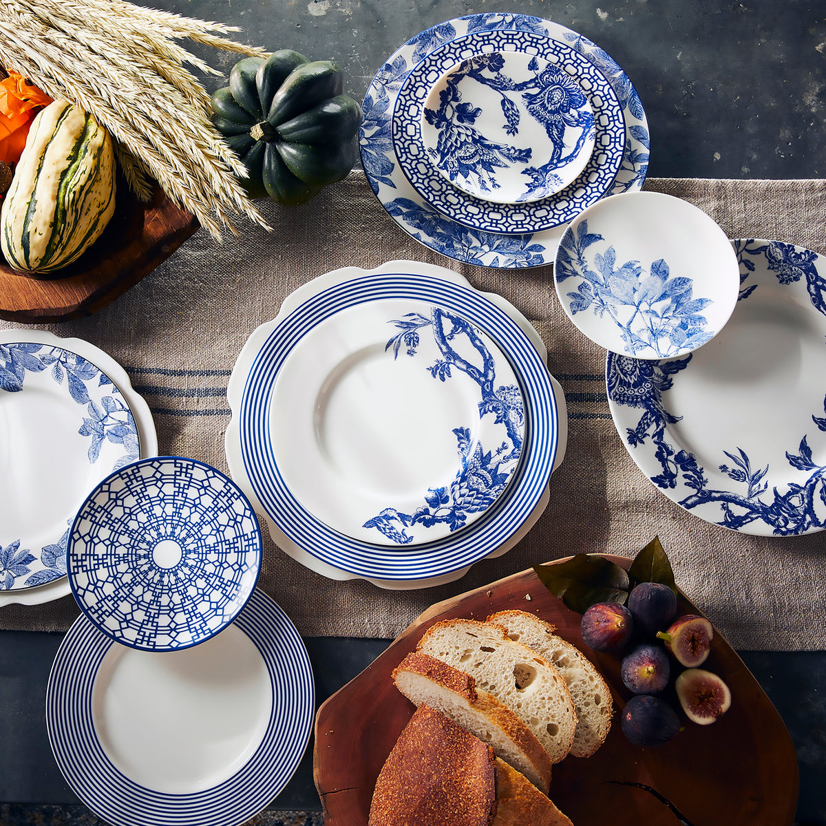 A Caskata Artisanal Home Newport Racing Stripe Rimmed Dinner Plate in blue and white adorned with fruit and bread.