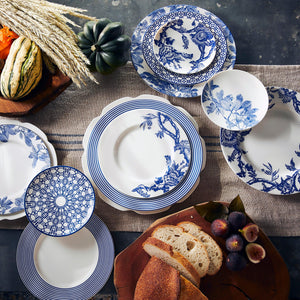 A variety of blue and white Newport Stripe Rimmed Dinner Plates from Caskata Artisanal Home are arranged on a table with bread, figs, wheat stalks, and gourds as decoration. The contemporary dinnerware adds a modern elegance to the rustic setting.