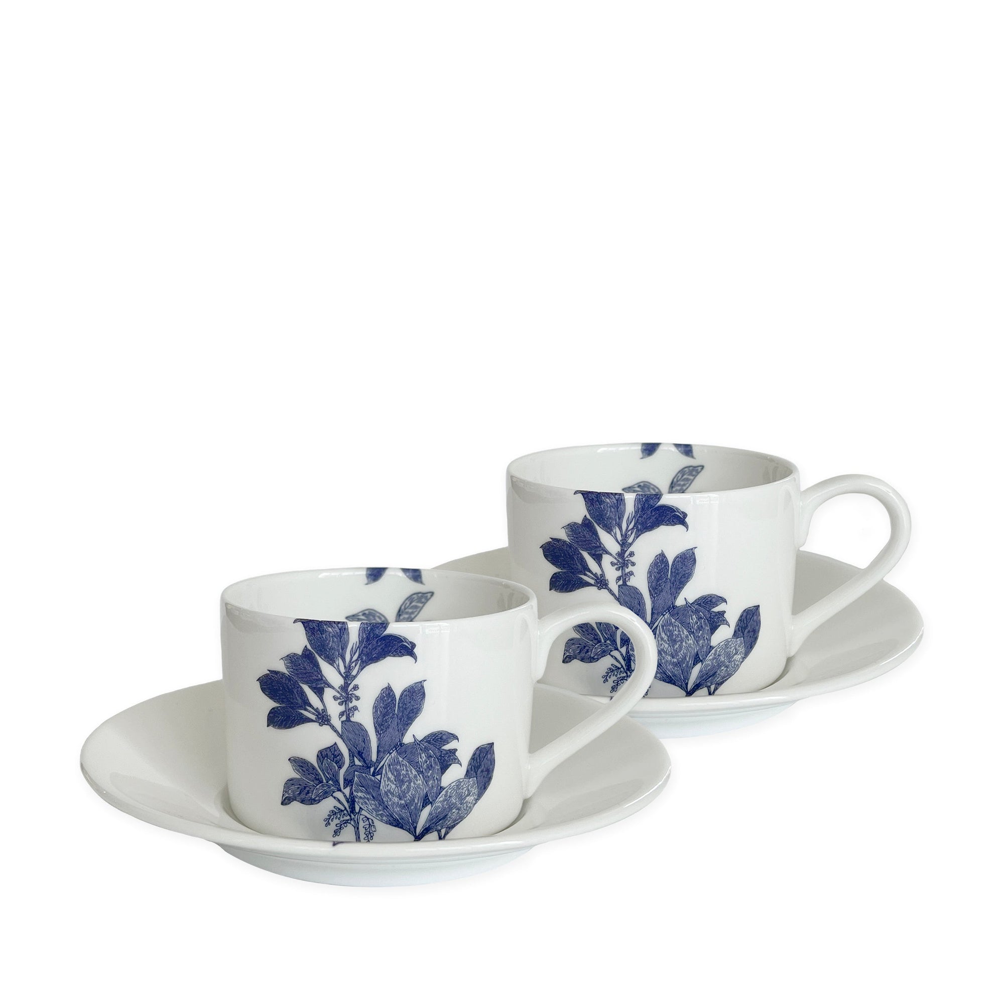 Two white bone china cups with matching saucers, decorated with blue floral patterns, are placed side by side against a white background. This elegant blue and white dinnerware, the Arbor Cups & Saucers, Set of 2 from Caskata Artisanal Home, is both dishwasher and microwave safe.