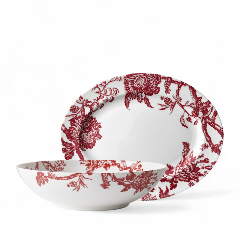 The Arcadia Crimson Serving Set by Caskata features white porcelain plates and bowls with vibrant red floral botanical designs—an elegant choice to enhance your holiday table for any occasion.