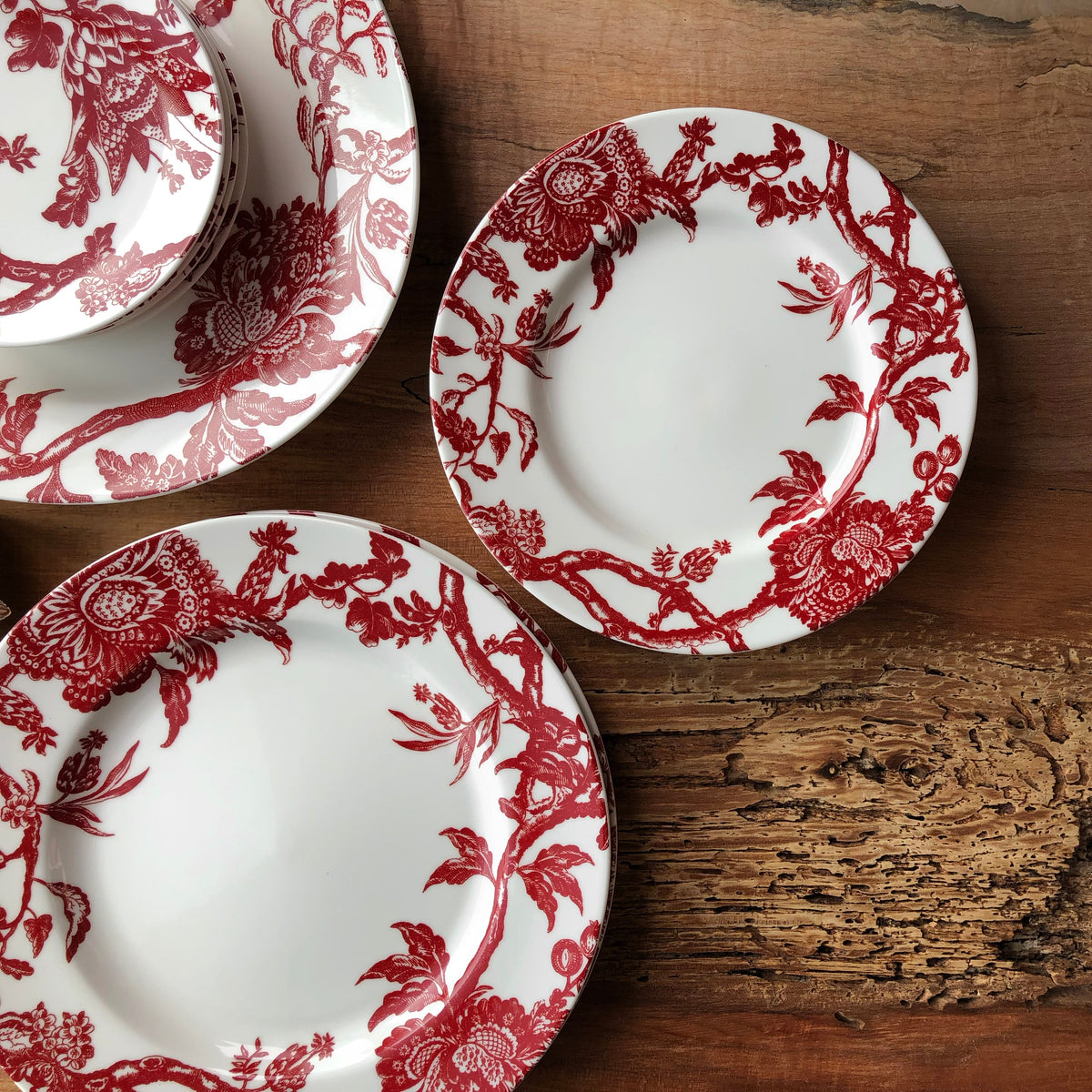 A set of Arcadia Crimson Rimmed Dinner Plates by Caskata Artisanal Home on a wooden table.