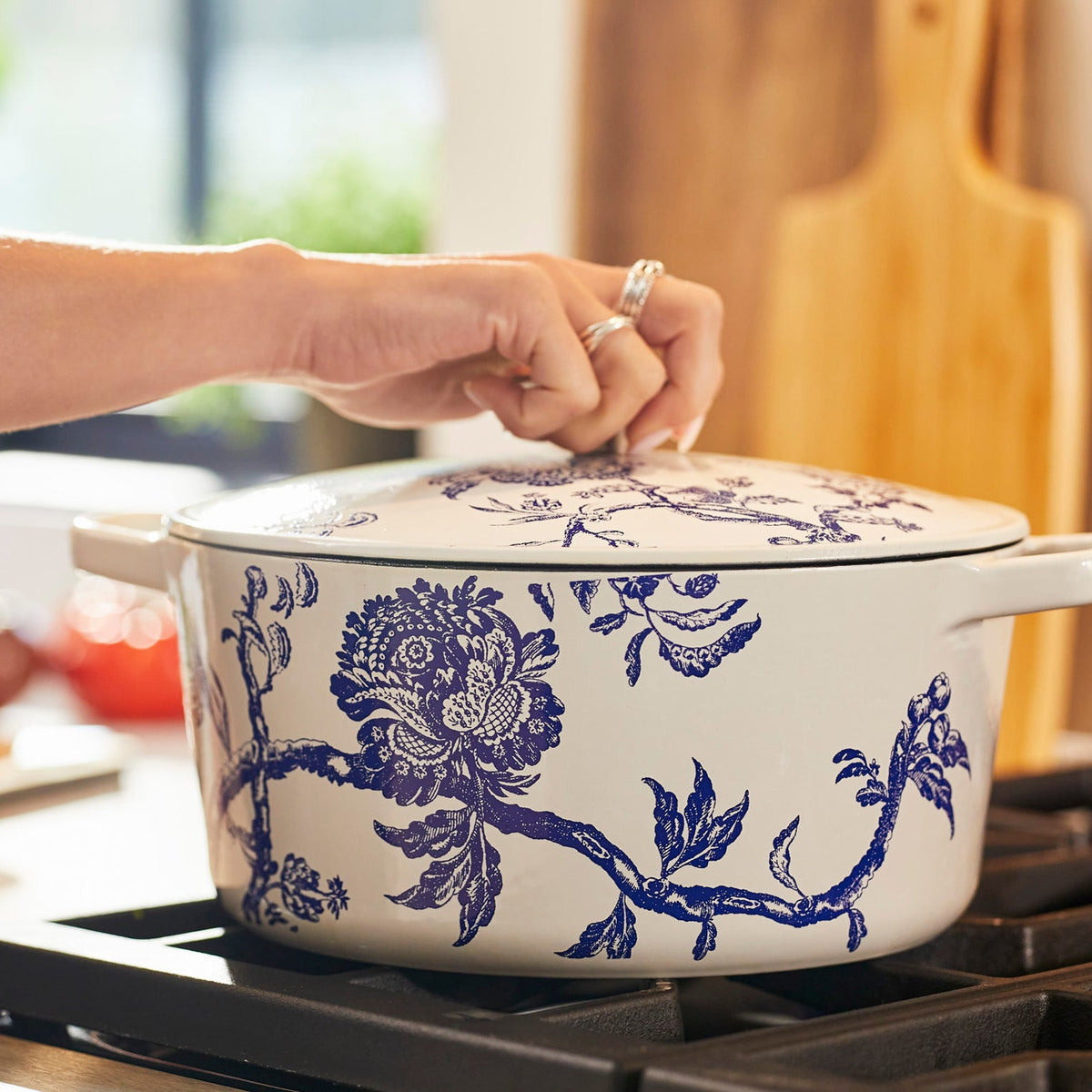 A person placing a Caskata X Cuisinart Limited Edition Arcadia Enameled Cast Iron 5 Qt. Round Casserole with Lid on a stove.