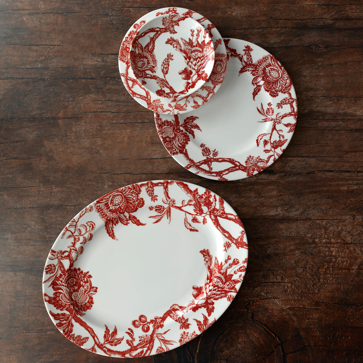 Three Arcadia Crimson Rimmed Dinner Plates by Caskata Artisanal Home on a wooden table.
