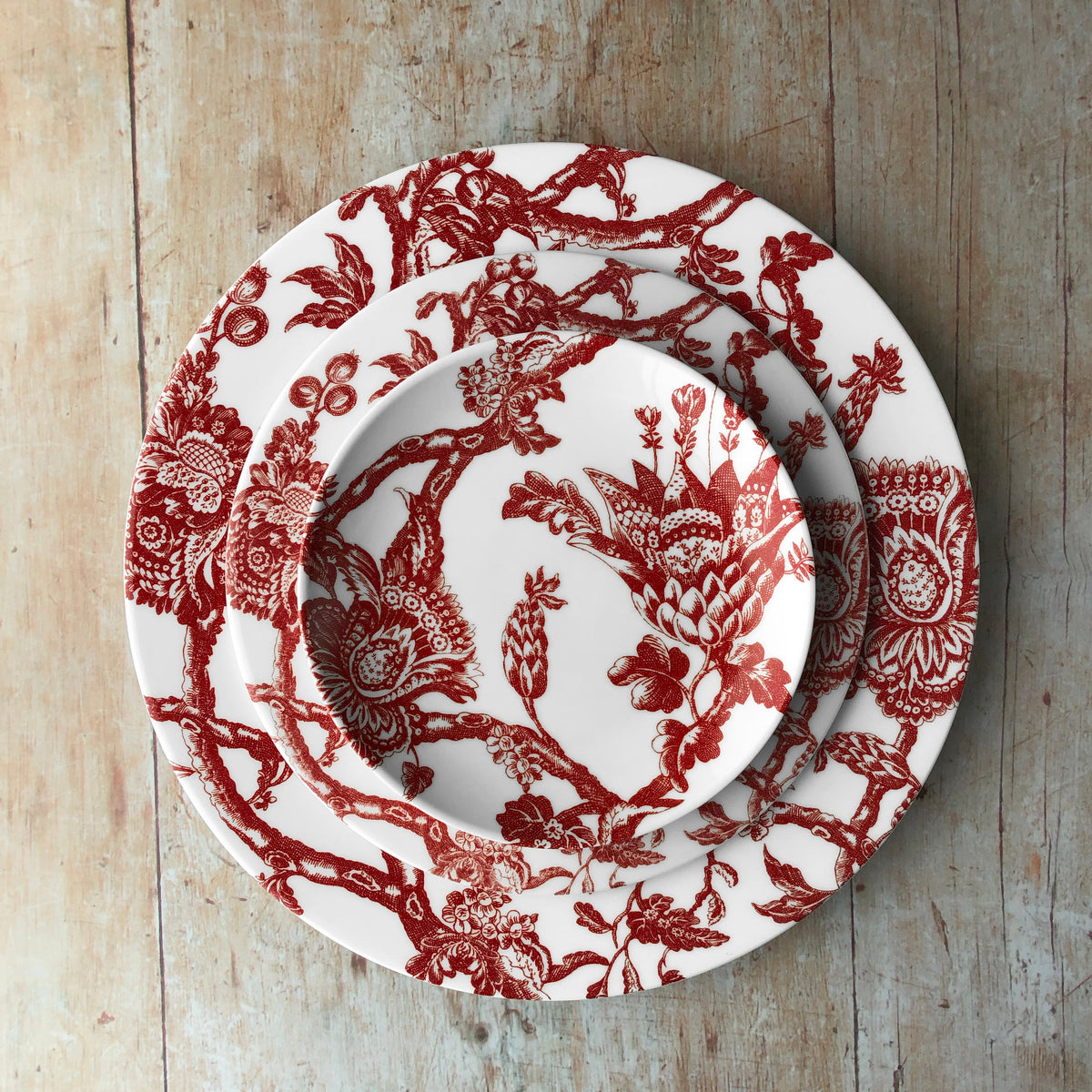 A set of Arcadia Salad Plate Crimson plates from the Caskata Artisanal Home porcelain collection on a wooden table.