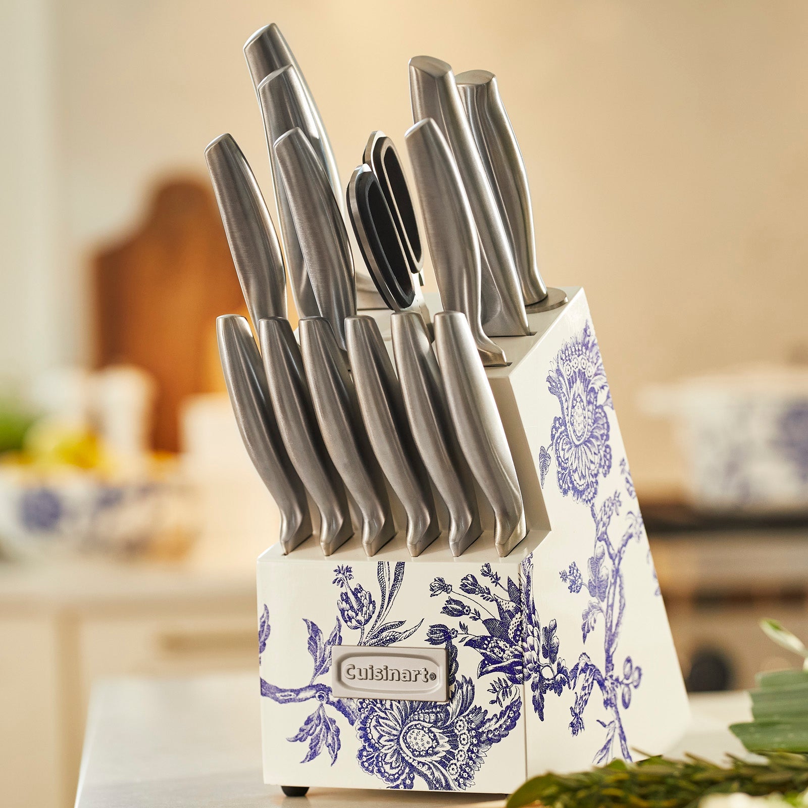 The Caskata X Cuisinart Limited Edition Arcadia 15-piece German Stainless Steel Cutlery Block, from Cuisinart, showcases knives with floral engravings on high carbon German stainless steel blades. The set includes several knives in a block adorned with a blue floral pattern, and two knives are displayed in front.
