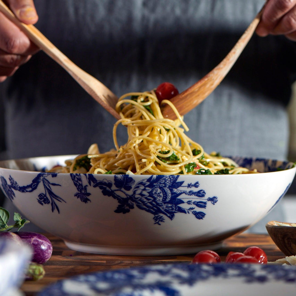 A person is holding an Arcadia Wide Serving Bowl by Caskata Artisanal Home over a serving bowl of pasta.