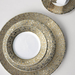 A set of three nested plates, including the Ellington Shimmer Gold & Platinum Bread & Butter Plate by Caskata Artisanal Home and a cup with saucer, all hand-decorated with a gold and silver circular pattern on a white background. This elegant harmony of design is both stunning and practical as each piece is dishwasher safe.