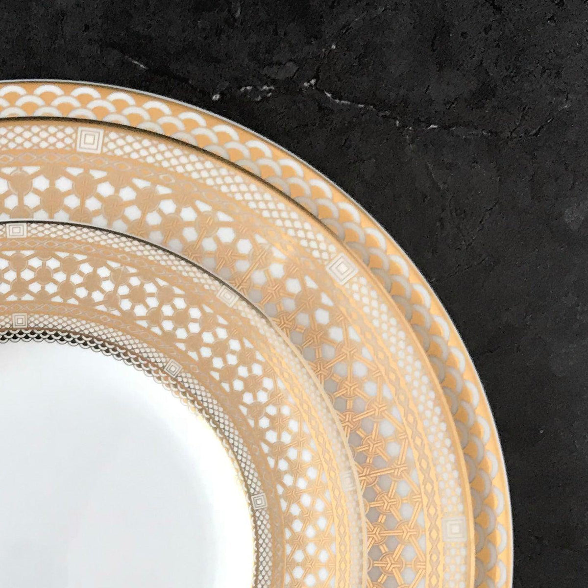 A Caskata Artisanal Home Hawthorne Gilt charger plate, made of bone china, showcased on a black surface.