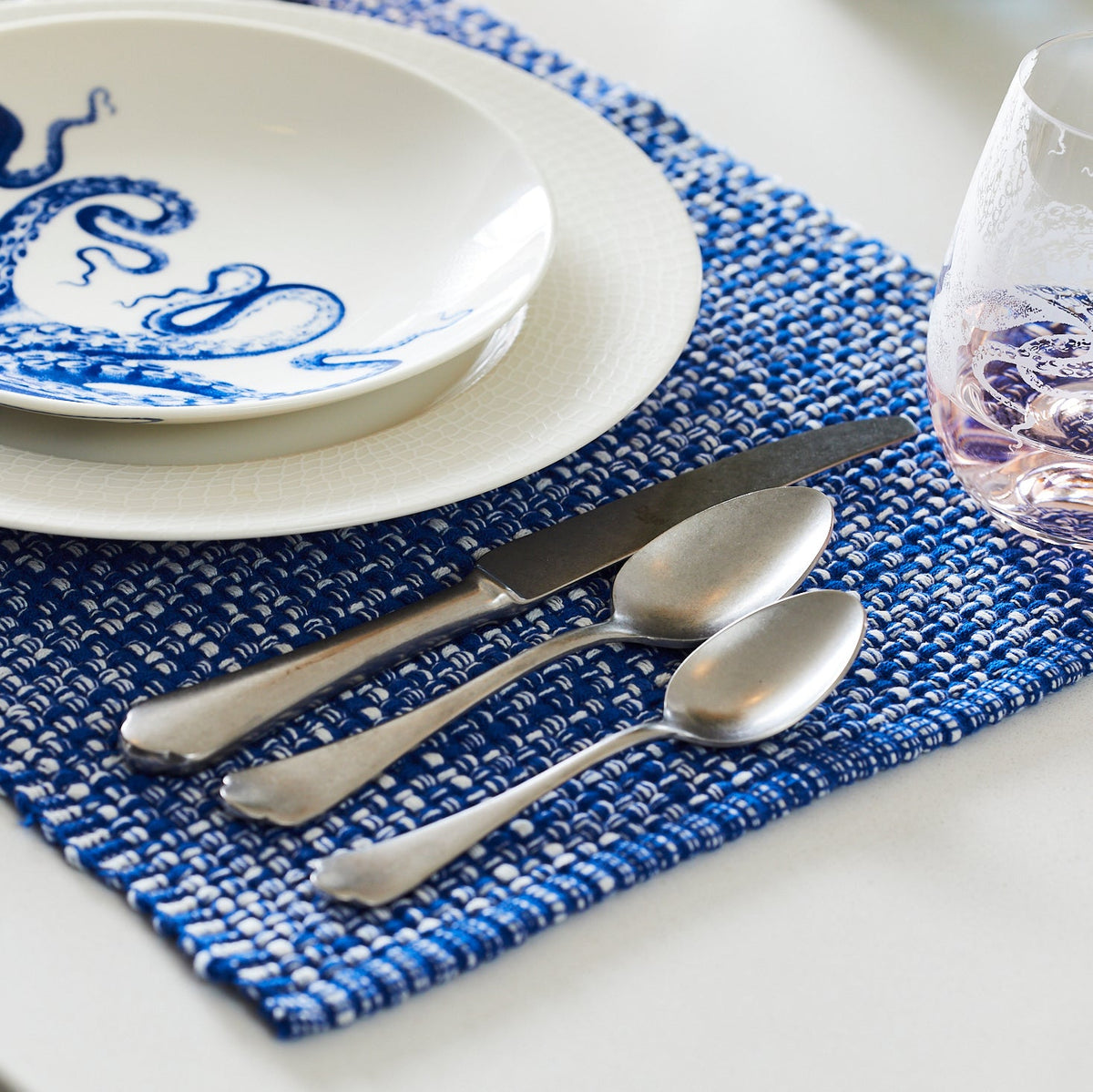 A blue and white Mepra Baroque Collection placemat with the Baroque 5-Piece Flatware Setting on it.