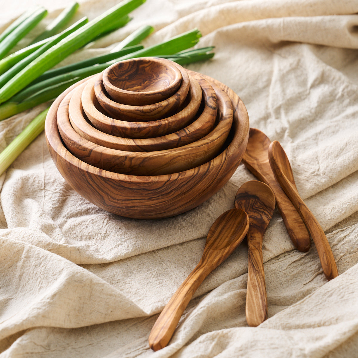 A handcrafted Be Home olive wood bowl with Olive Wood Small Spoons, Set of 4 and green onions.