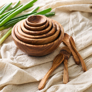 A handcrafted Be Home olive wood bowl with Olive Wood Small Spoons, Set of 4 and green onions.