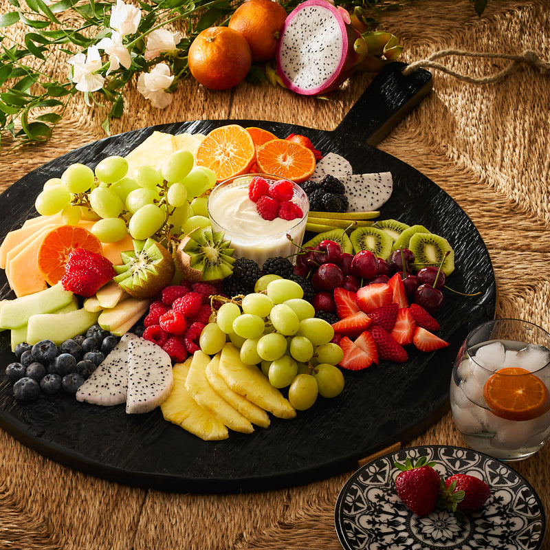 Assorted fresh fruits neatly arranged on a Black & Natural Round Charcuterie Big Board with a side of cream, all coated in a 100% plant-based, food-safe wax finish by Etu Home.