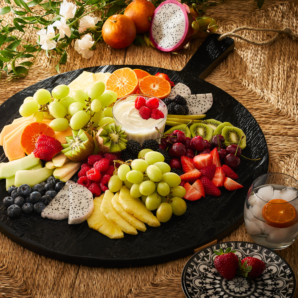 Assorted fresh fruits neatly arranged on a Black &amp; Natural Round Charcuterie Big Board with a side of cream, all coated in a 100% plant-based, food-safe wax finish by Etu Home.