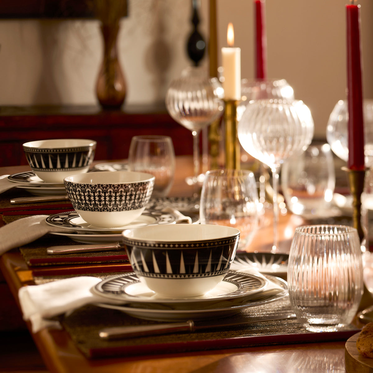 The Marrakech Table for 8 by Caskata features black and white Art Deco dishes, glassware, cutlery, white napkins, and candles arranged on a dining table in a warm, inviting setting.
