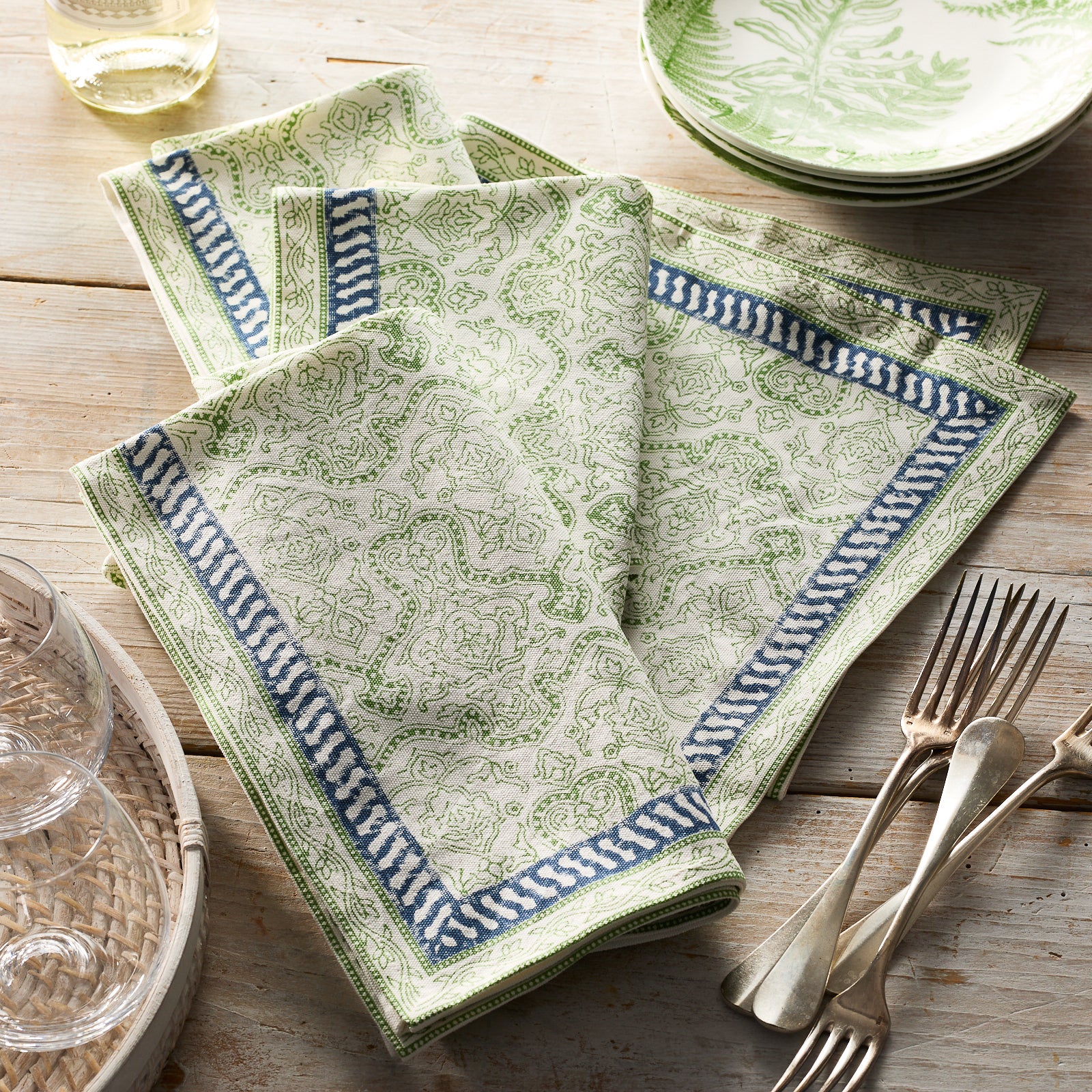 Four folded Block Island Block Print Dinner Napkins by Caskata in white, featuring a green intricate pattern and blue-white border—a charming choice for bohemian table decor.