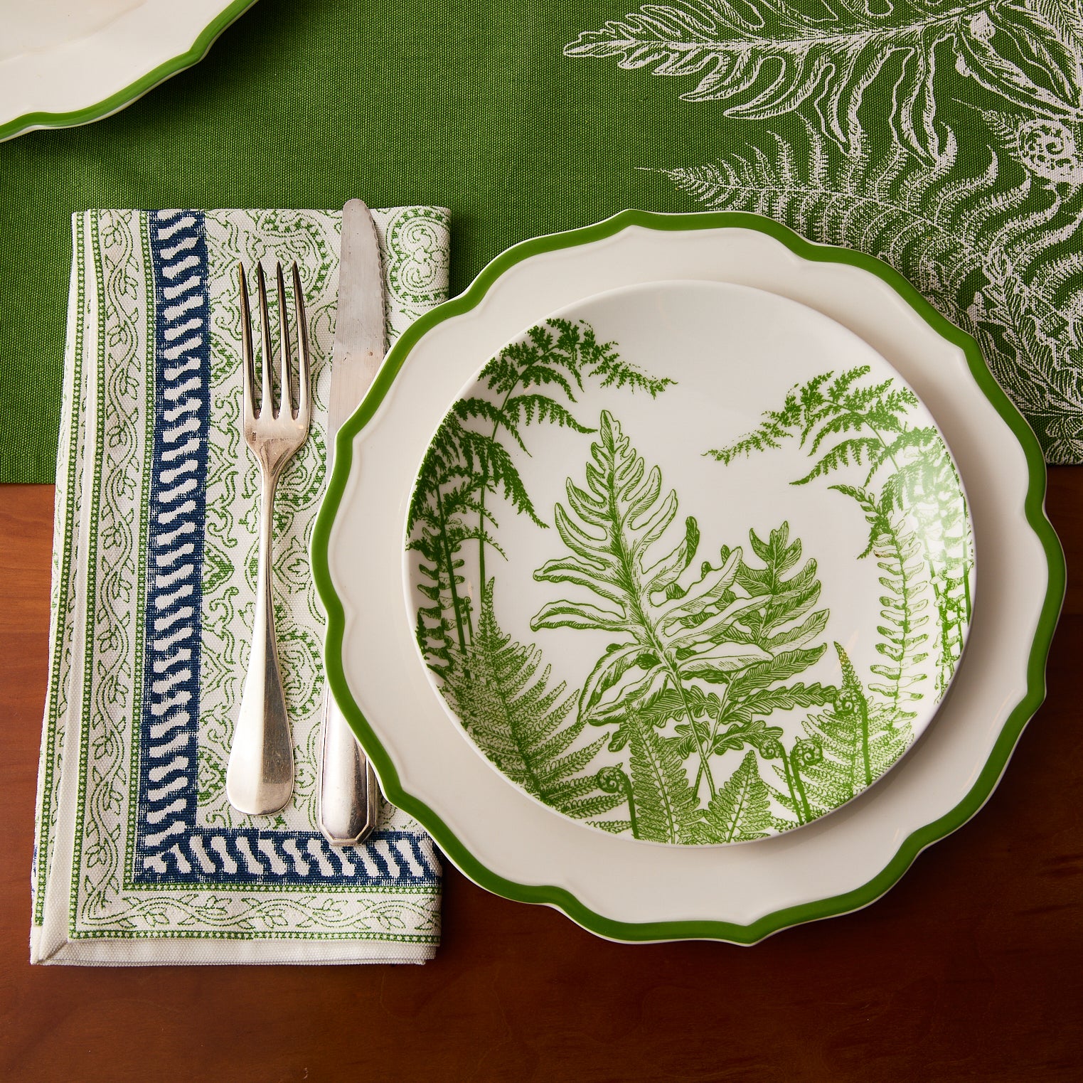 Four folded Block Island Block Print Dinner Napkins by Caskata in white, featuring a green intricate pattern and blue-white border—a charming choice for bohemian table decor.