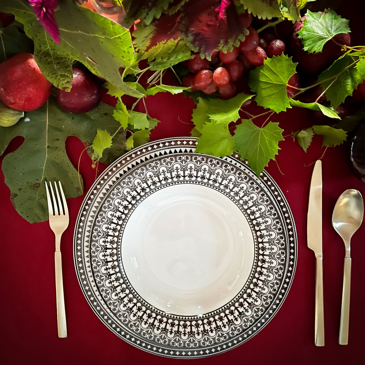 Elegant table setting with Casablanca Rimmed Soup Bowls from the Caskata Artisanal Home Geometrics Collection on a red tablecloth, surrounded by fresh fruits and foliage.