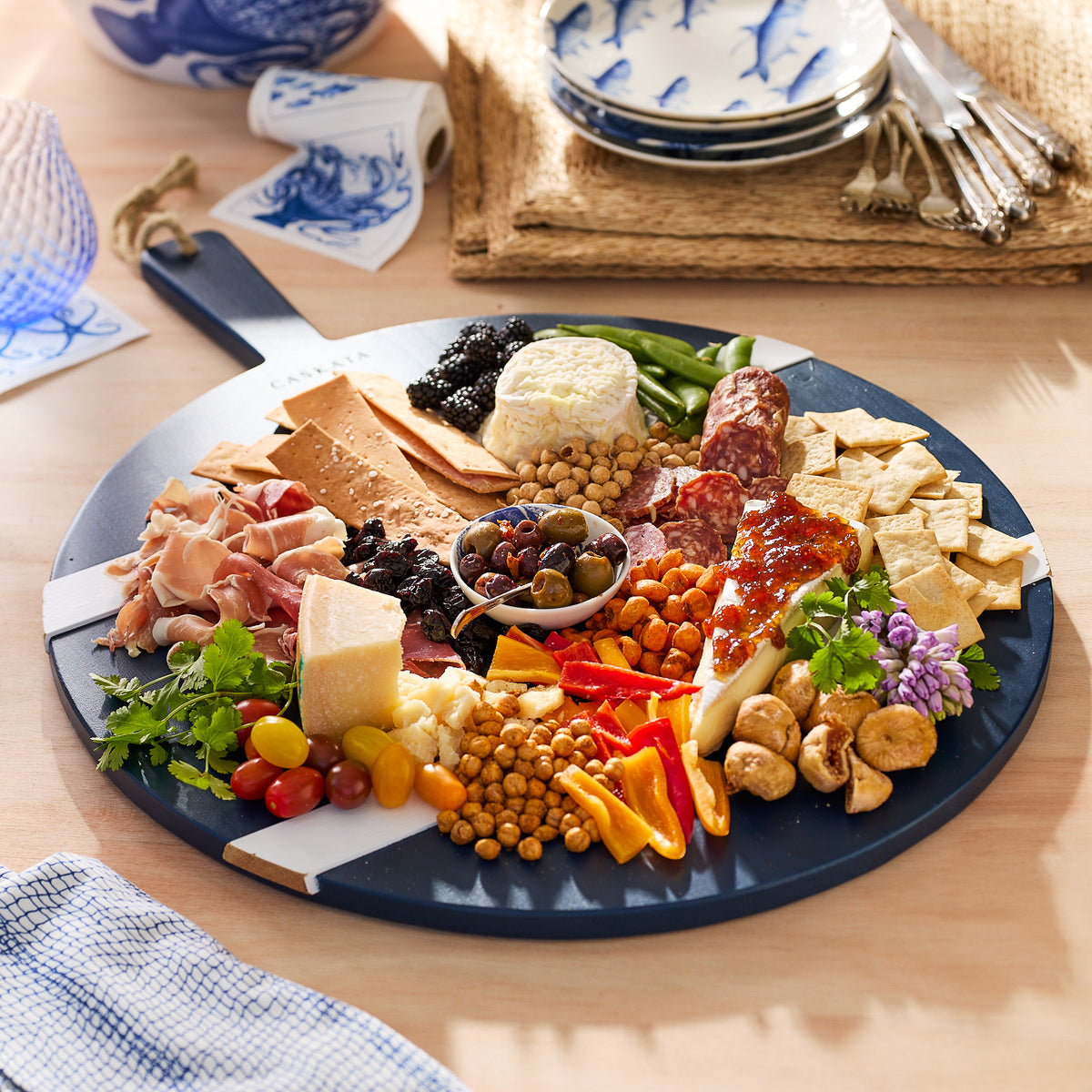 A well-presented Navy and White Round Charcuterie Big Board, crafted from reclaimed European timbers and finished with a food-safe wax, holds a variety of cheeses, cured meats, crackers, and accompaniments on a Etu Home.