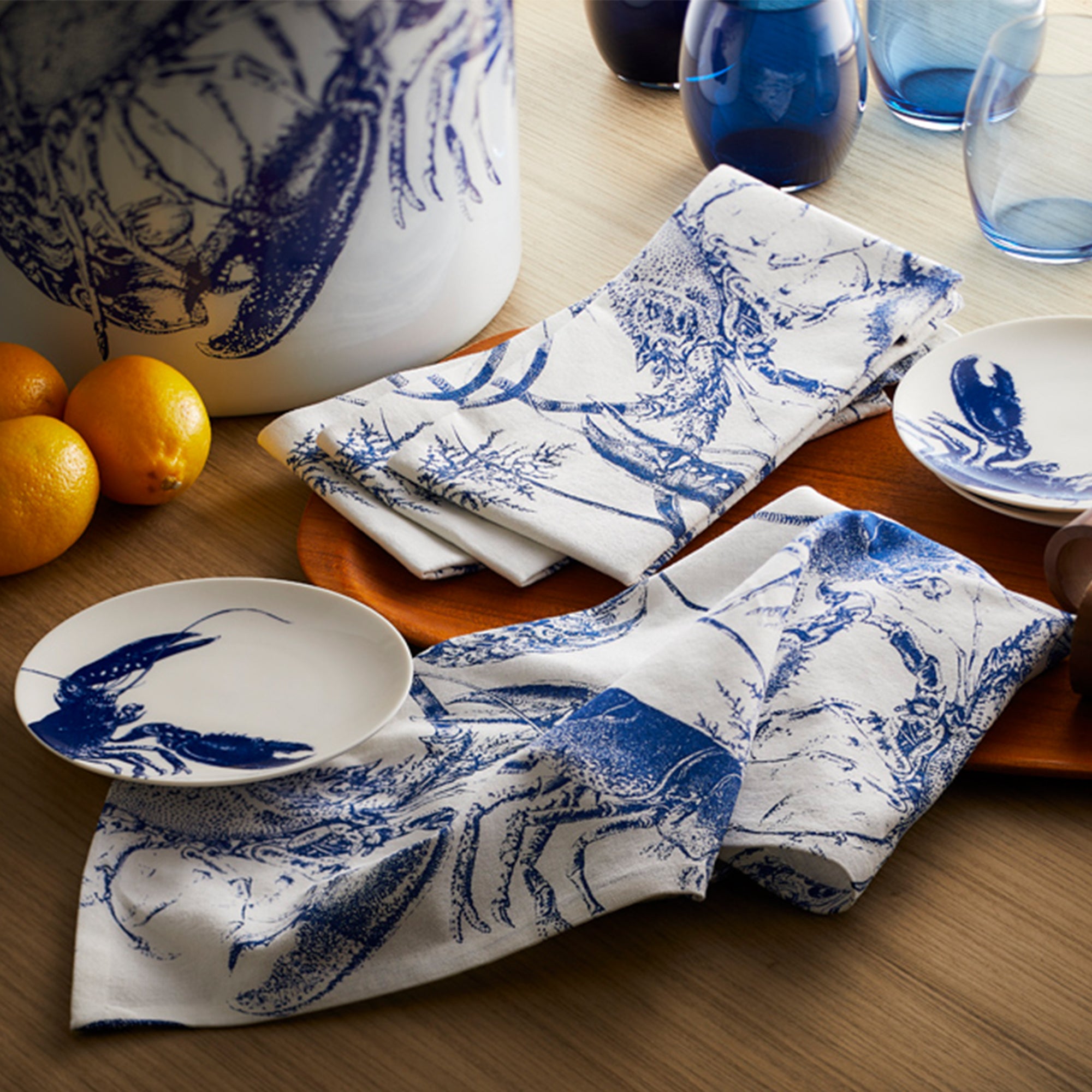 The Caskata Blue Lobster Dinner Napkins set includes four 100% cotton napkins, each featuring charming blue lobster illustrations elegantly arranged.