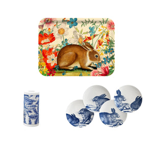 The Caskata Blue Bunnies Bundle features a birchwood serving tray with a rabbit and flowers, four round plates with blue rabbits, and a blue-and-white paper towel roll—an eco-friendly set perfect for spring entertaining.