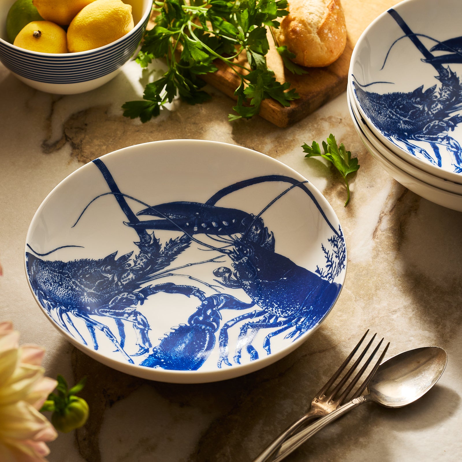 The Caskata Lobster Entrée Bowl is a white porcelain bowl featuring a blue, nature-inspired design inside. This elegant bowl is also dishwasher safe.