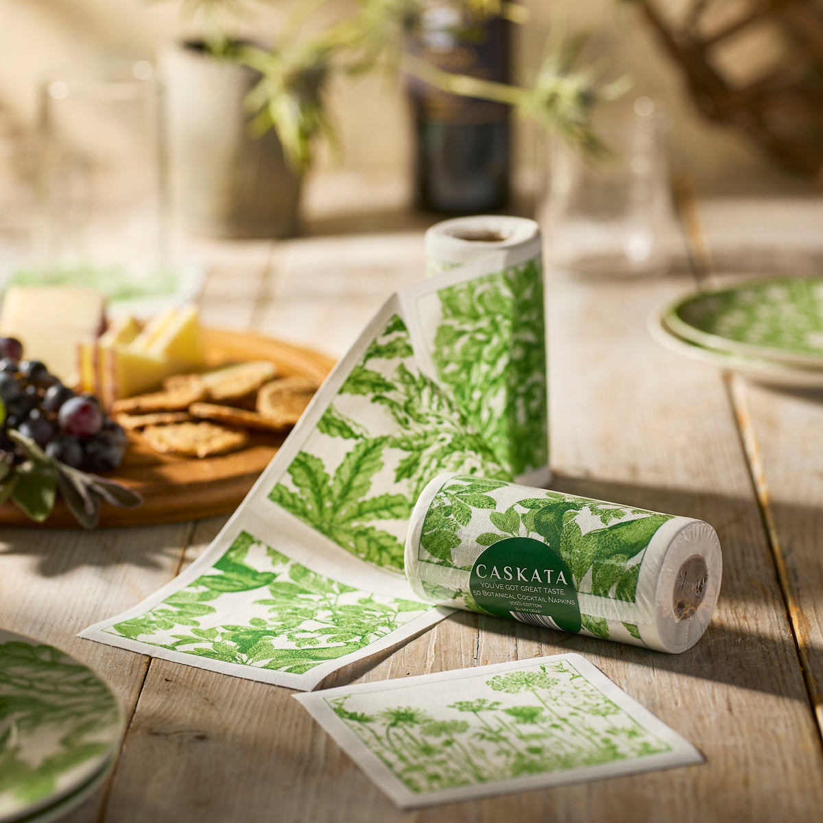 The MY DRAP Botanicals Verde Cocktail Napkin Roll is unrolled on a wooden table set with plates, cheese, crackers, and grapes.
