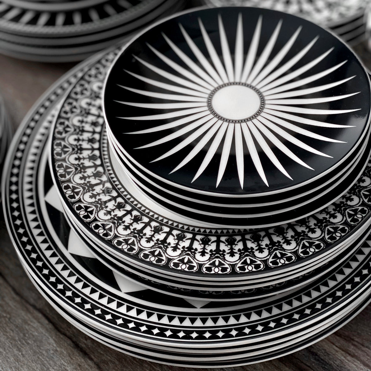 A stunning Geometrics Collection 60 Pc. Set by Caskata Artisanal Home, featuring black and white plates adorned with Moroccan-inspired and graphic patterns, elegantly stacked on top of each other.