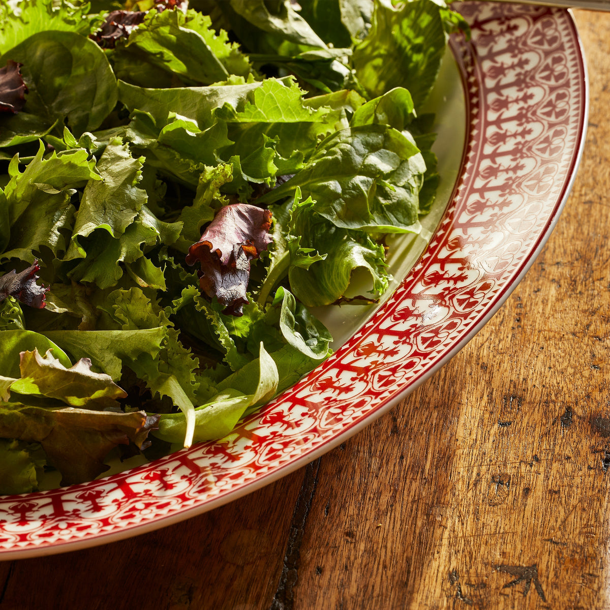 Closeup of Caskata&#39;s Casablanca Crimson Rimmed Platter shows the detail of the rich red pattern against bright salad greens.