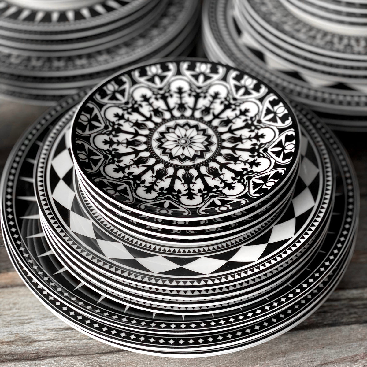 Stacked black and white plates featuring Moroccan-inspired patterns from Caskata Artisanal Home&#39;s Geometrics Collection 60 Pc. Set.
