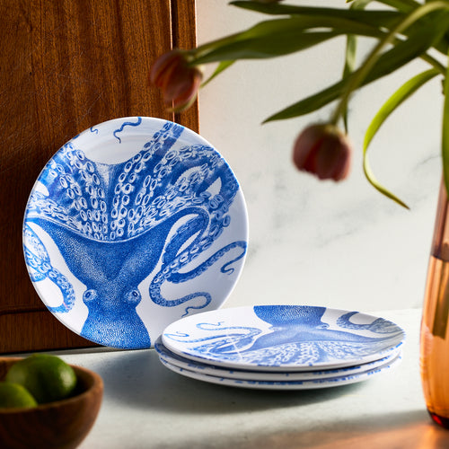 The Lucy "Party Pack" Melamine Bundle by Caskata is stacked beside a wooden board, with tulips in a vase and bright green limes surrounding it.
