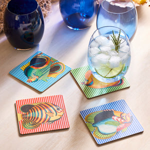 The Party Fish Birchwood Coasters by Caskata, a set of four vibrant and eco-friendly trays, lay on the table like a party under the sea. A cooling iced drink sits on one coaster, while nearby three blue glasses await the fun. Perfect for adding charm and eco-consciousness to any gathering!.