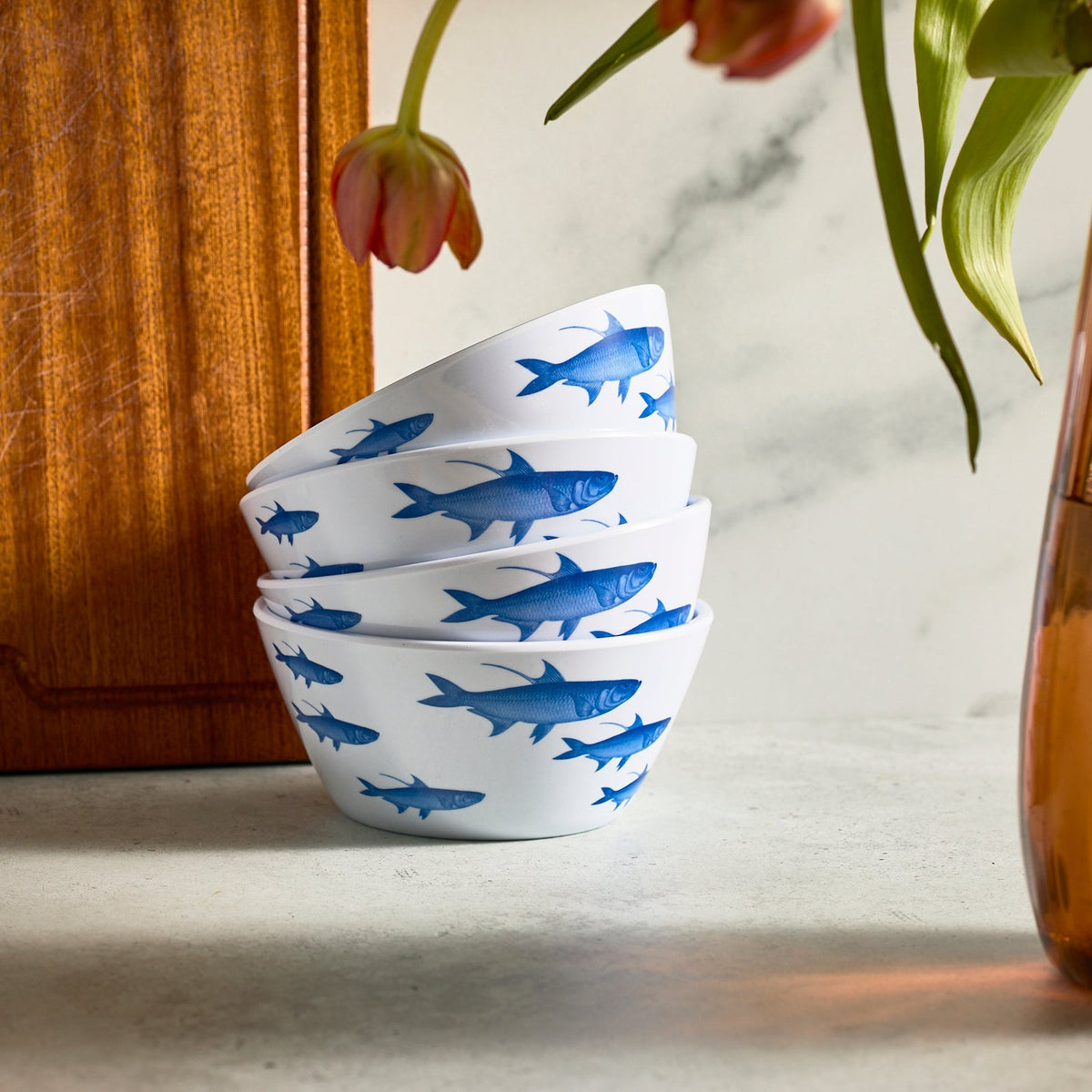 Caskata's School of Fish Melamine Cereal Bowls, set of 4, add a coastal flair on a marble surface beside a vase of pink and orange tulips.