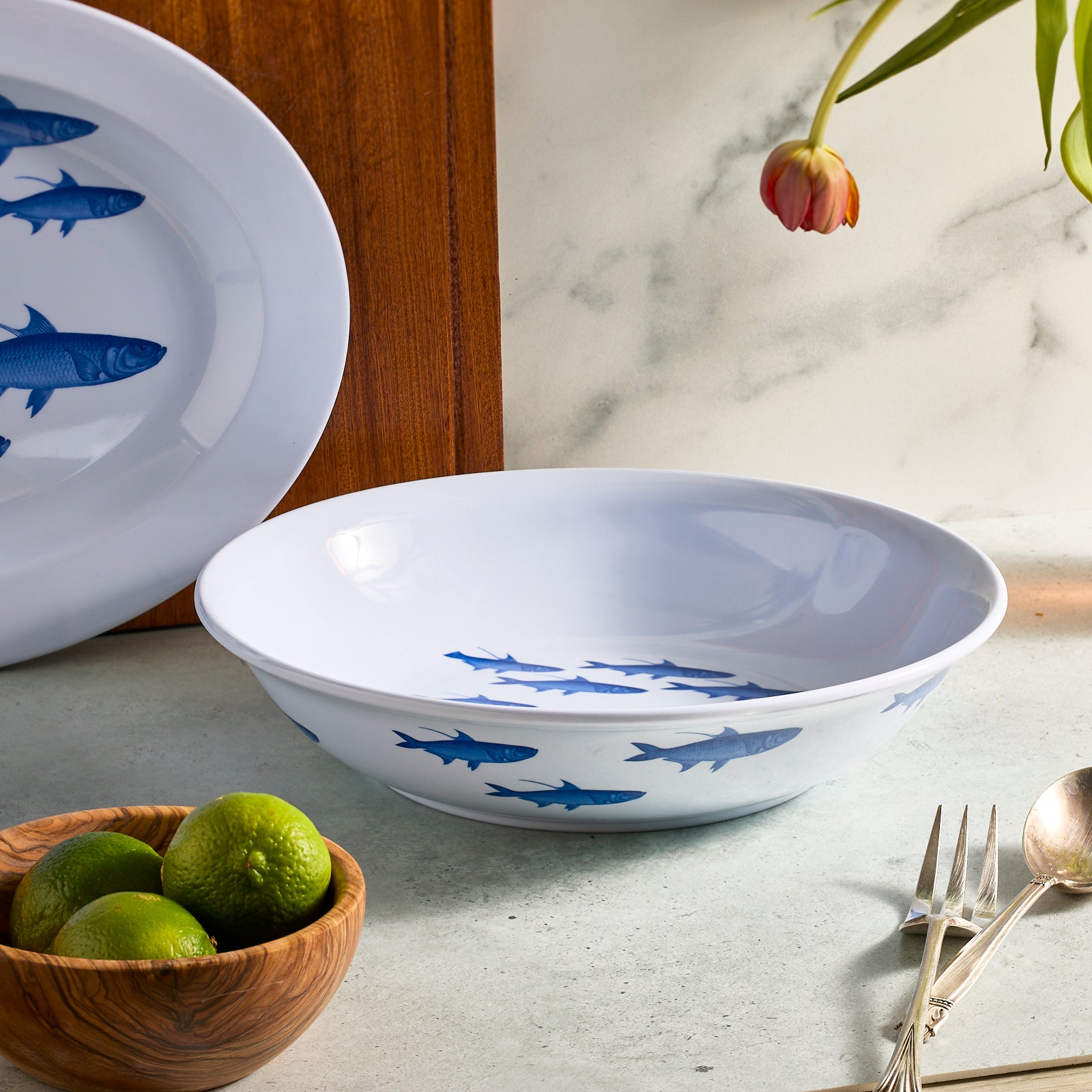 The Caskata School of Fish Melamine Serving Bowl showcases blue fish swimming elegantly in unison on a white surface, perfect for adding whimsy to outdoor gatherings.