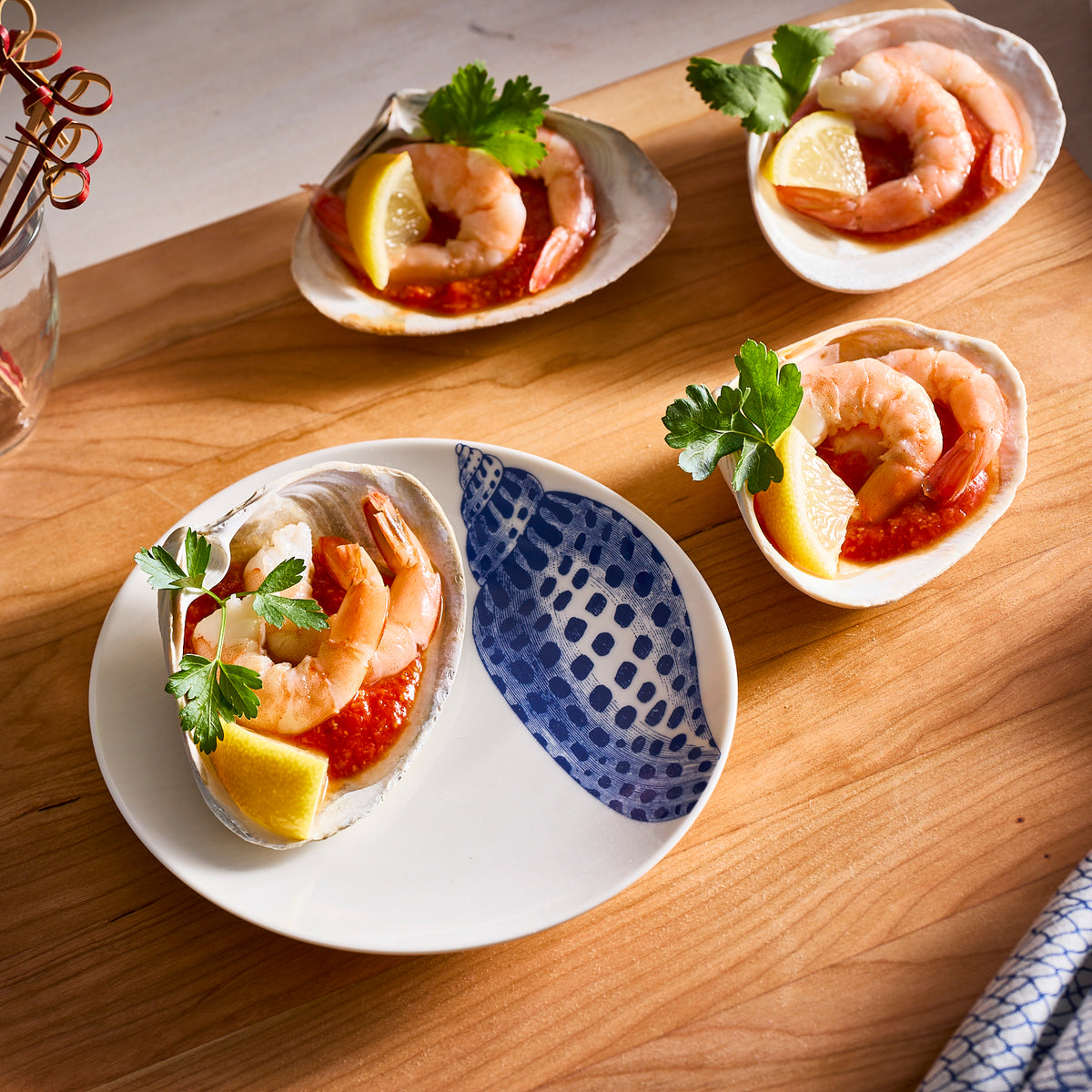 Four shrimp cocktails presented on Caskata Artisanal Home&#39;s Shells Small Plates, with cocktail sauce, lemon wedges, and parsley beautifully arranged on a wooden surface—an entertaining powerhouse.