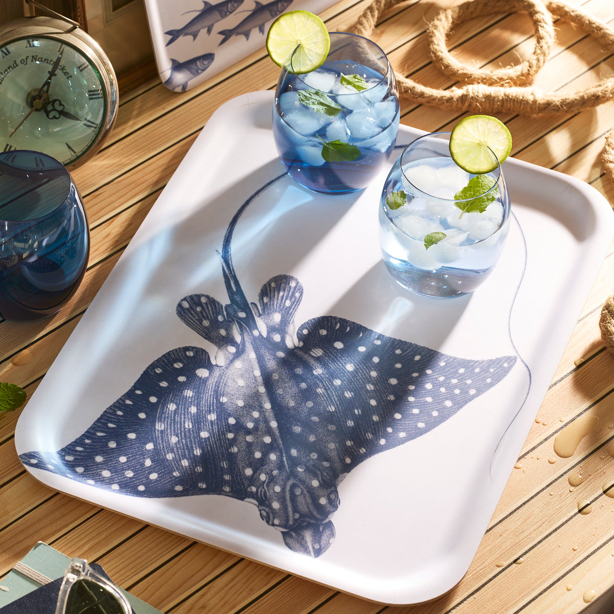 Two glasses with ice, lime, and mint are on the Spotted Stingray Large Rectangular Birchwood Tray by Caskata from the Coastal Collection, resting on a wooden surface with nautical decor.