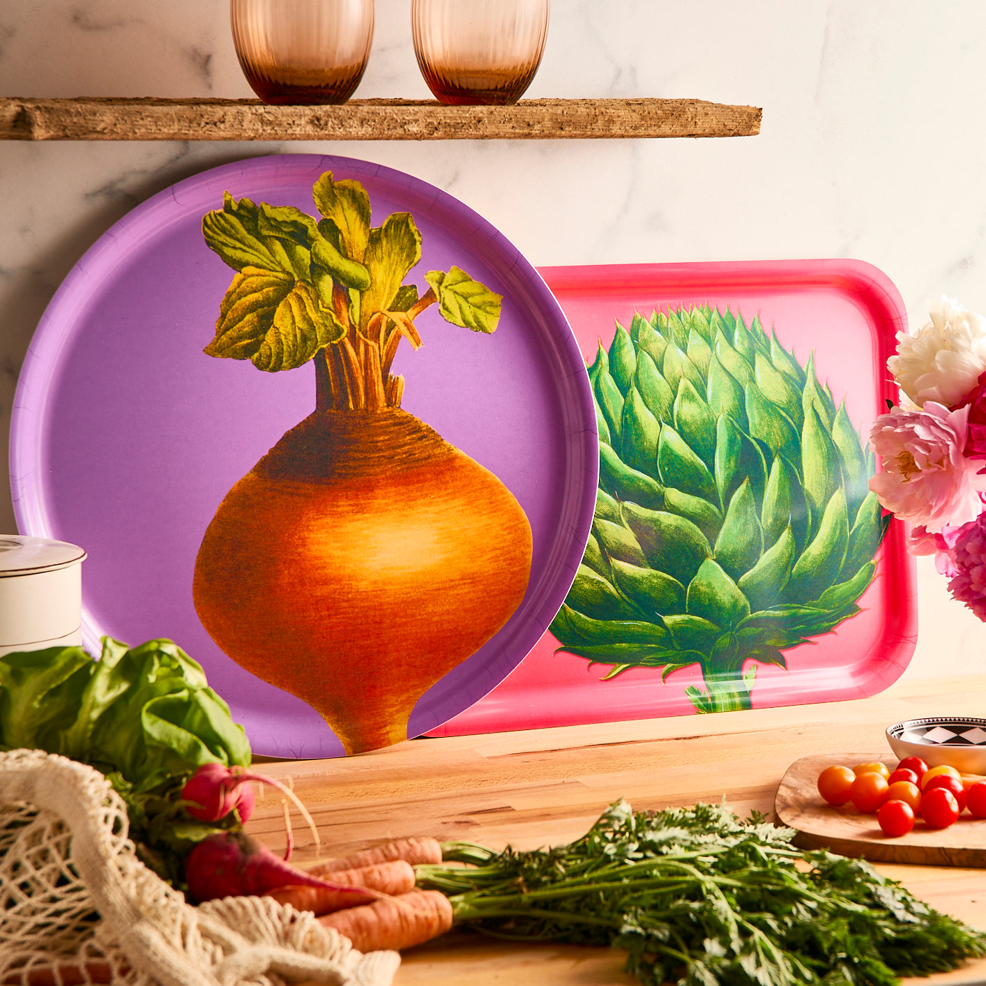 The Caskata Veggies Decorator Set features bright, colorful serving trays: a rectangular birchwood tray with an artichoke on pink and a round tray with a beet on purple—perfect decorative pieces for your home.