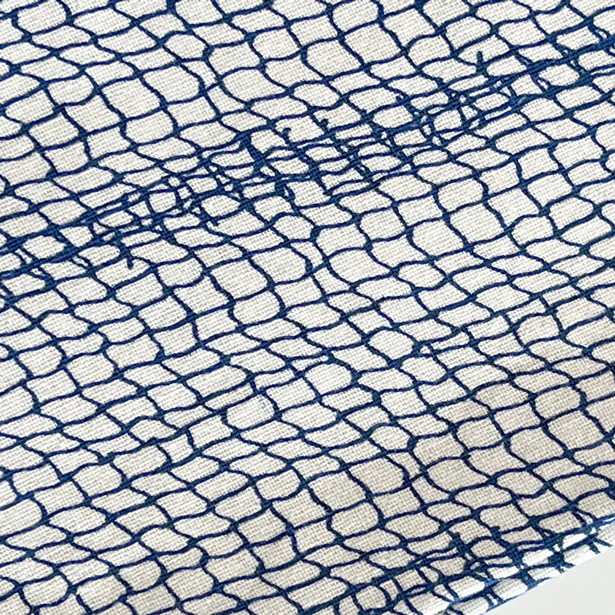 Close-up of 100% cotton fabric with an irregular blue grid pattern resembling a coastal design. A horizontal blue thread seam runs across the center, perfect for Caskata Catch Dinner Napkins, Set of 4.