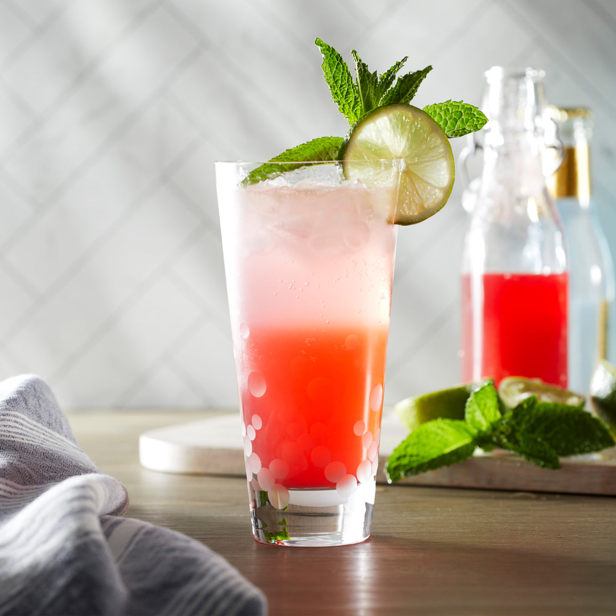 A pink drink with lime and mint leaves in Chatham Pop Highball Glasses by Caskata on a lead-free crystal cutting board.
